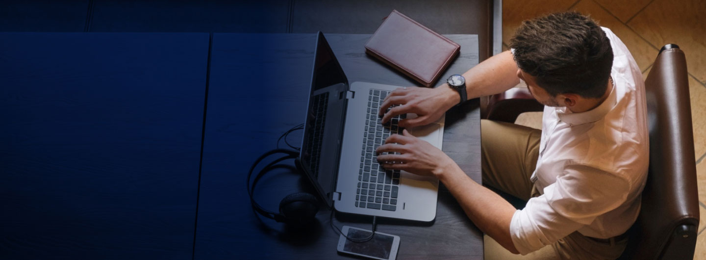 Profesional trabajando con portátil, cuaderno y móvil sobre la mesa.